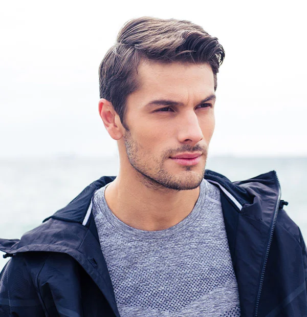 Sharp-dressed man standing outdoors, gazing confidently at the horizon with an ocean view behind him - Buccal Fat Removal in Portsmouth, NH