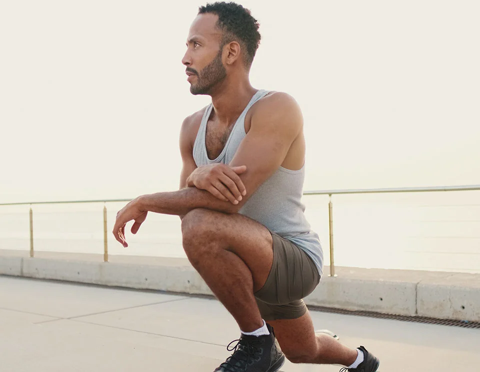 Man in workout clothes kneeling on a boardwalk, focused and ready for physical activity, with a calm ocean backdrop - Calf Implants in Portsmouth, NH