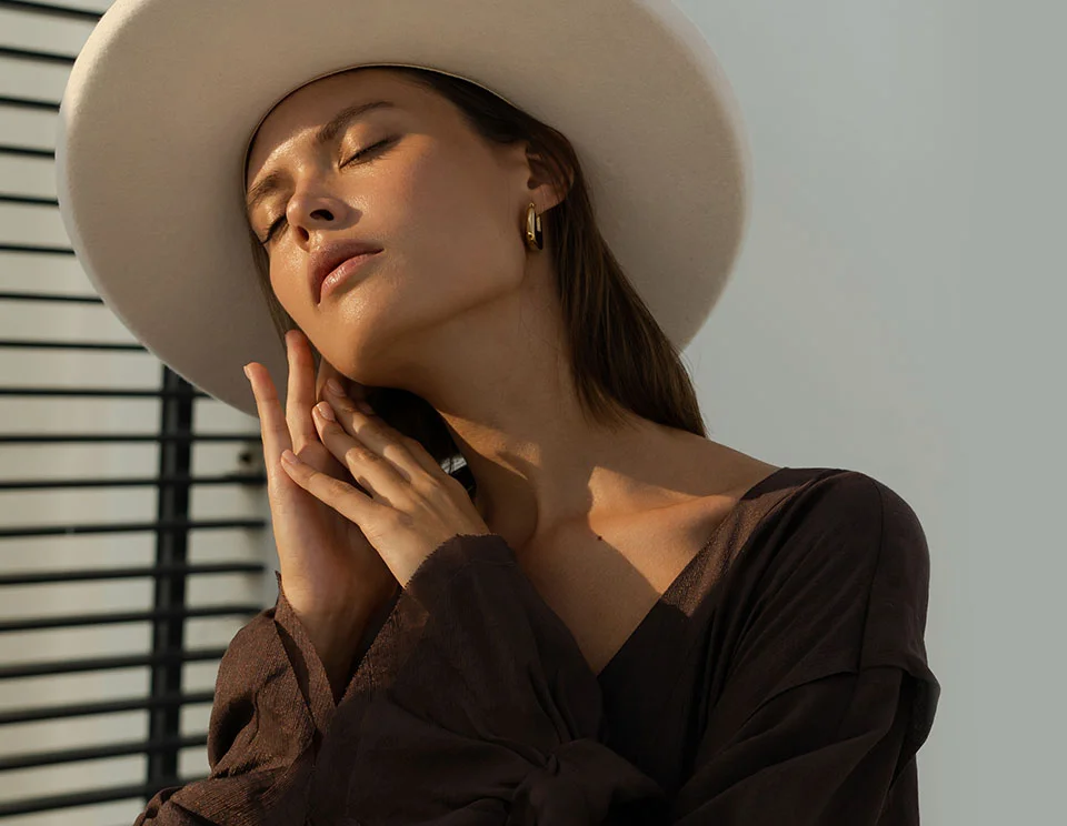 Elegant woman in a wide-brimmed hat, with eyes closed, basking in soft sunlight and embracing a moment of serenity - Chemical Peels in Portsmouth, NH