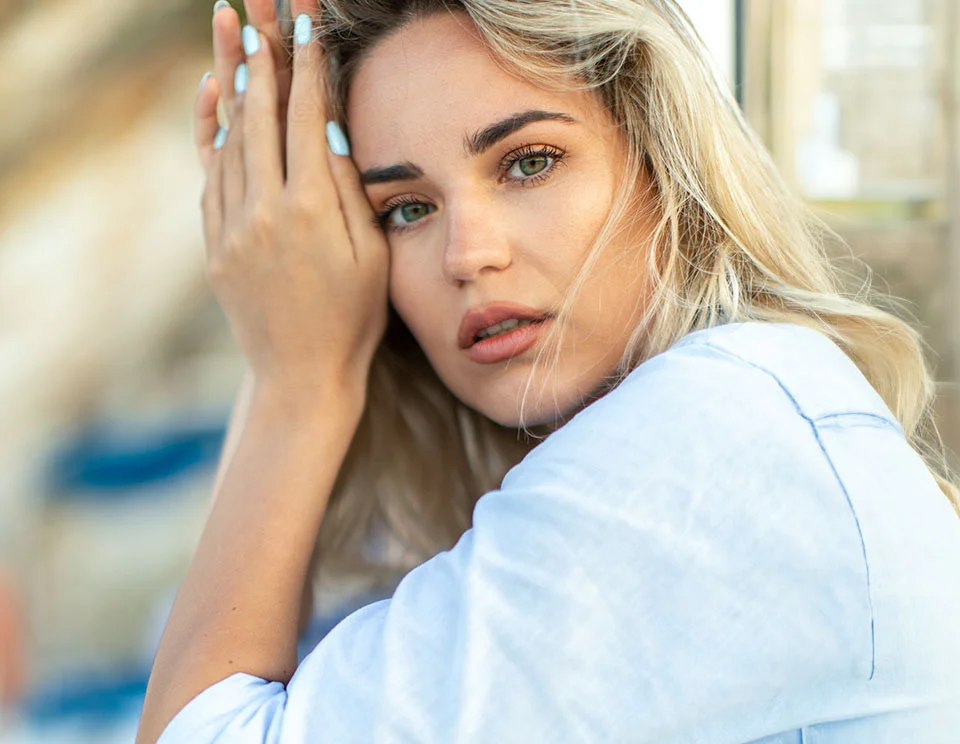 Blonde woman resting her hand on her face, looking directly at the camera with a serene expression, wearing light-colored clothing - Sofwave in Portsmouth, NH